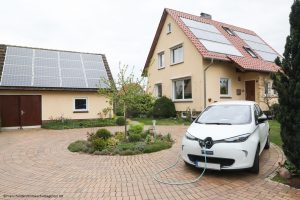 Eine Photovoltaikanlage auf dem Dach, ein Stromspeicher im Keller und ein Elektroauto vor der Tür, geladen mit regenerativer Sonnenenergie 